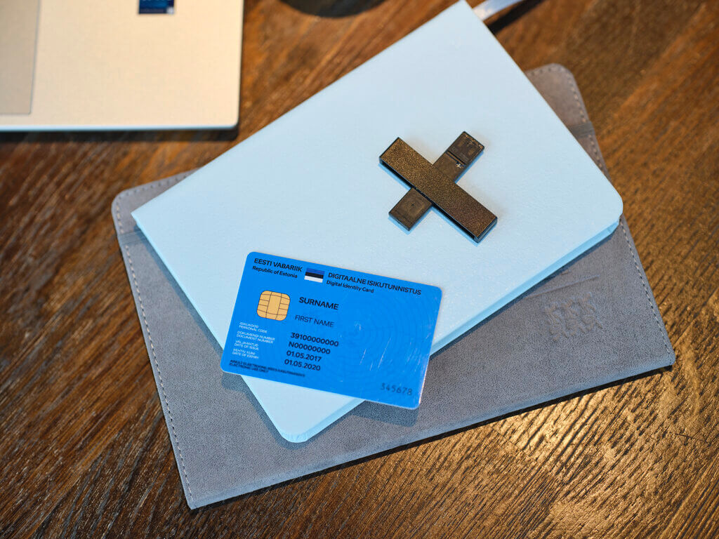 Blue e-Residency digital identity card and USB card reader lying on notebooks